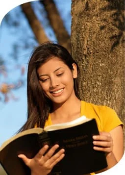 A woman engrossed in a book, sitting in front of a majestic tree, enjoying the serenity of nature.